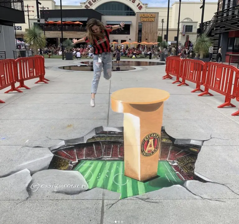 A woman leaps over a 3D chalk drawing of a gold Atlanta United pillar rising from a cracked hole that opens onto a soccer stadium.