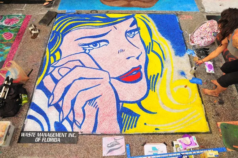 Chalk painting after Roy Lichtenstein's Crying Girl: a blonde woman with tears on her cheek and her hand at her mouth, in bright yellow, blue and red with dotted skin.