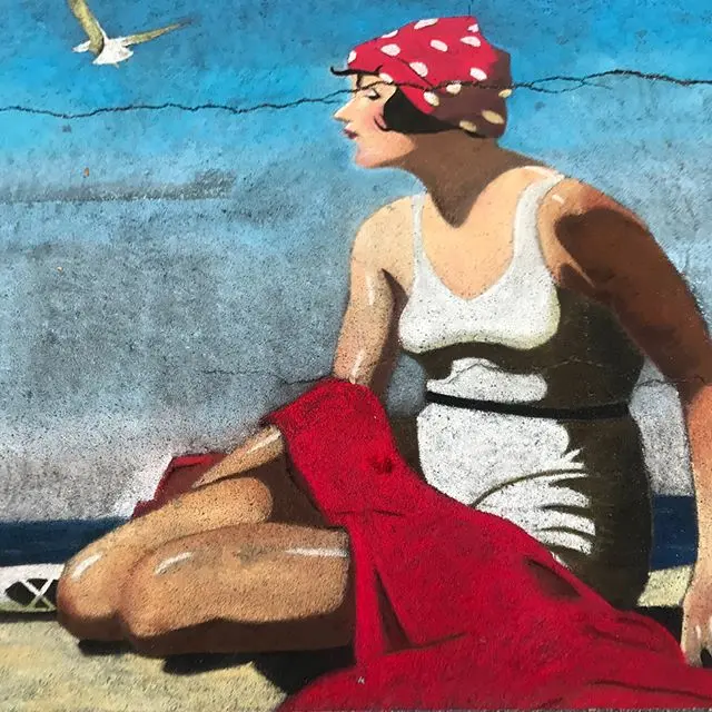 Chalk painting of a woman in a vintage swimsuit and red polka-dot head scarf sitting on a red towel by the sea as a gull flies overhead.
