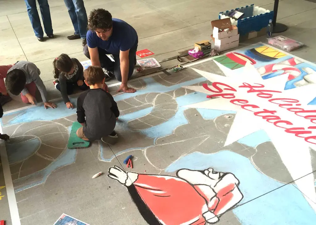 Families kneel to color a large holiday chalk piece on the floor at Ponce City Market.