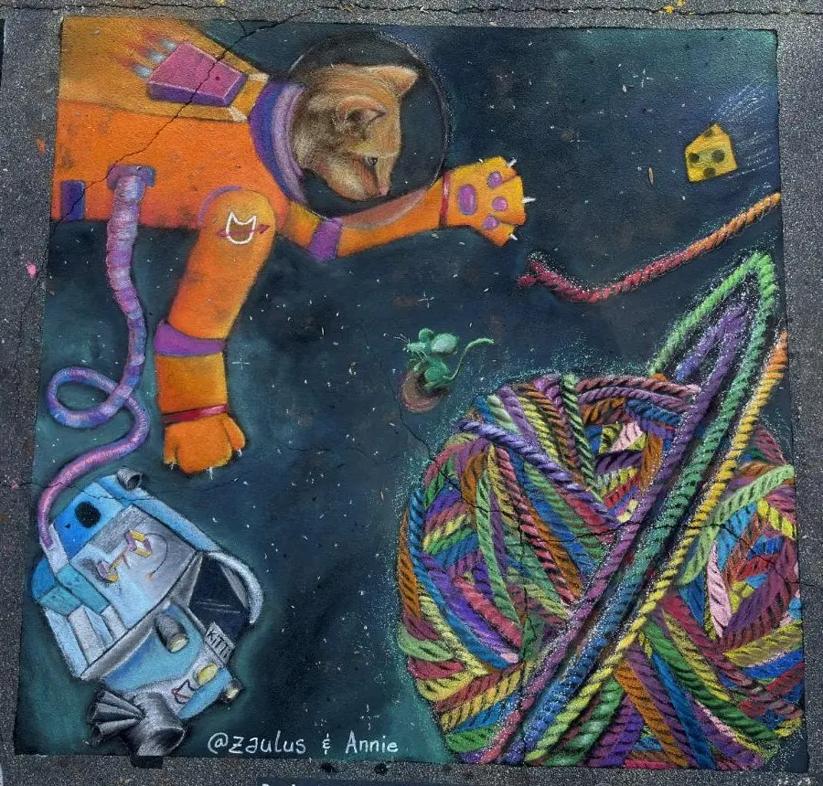 Chalk drawing of an orange cat in a spacesuit reaching for a floating ball of rainbow yarn, with a mouse, a piece of cheese and a small spacecraft drifting through space.
